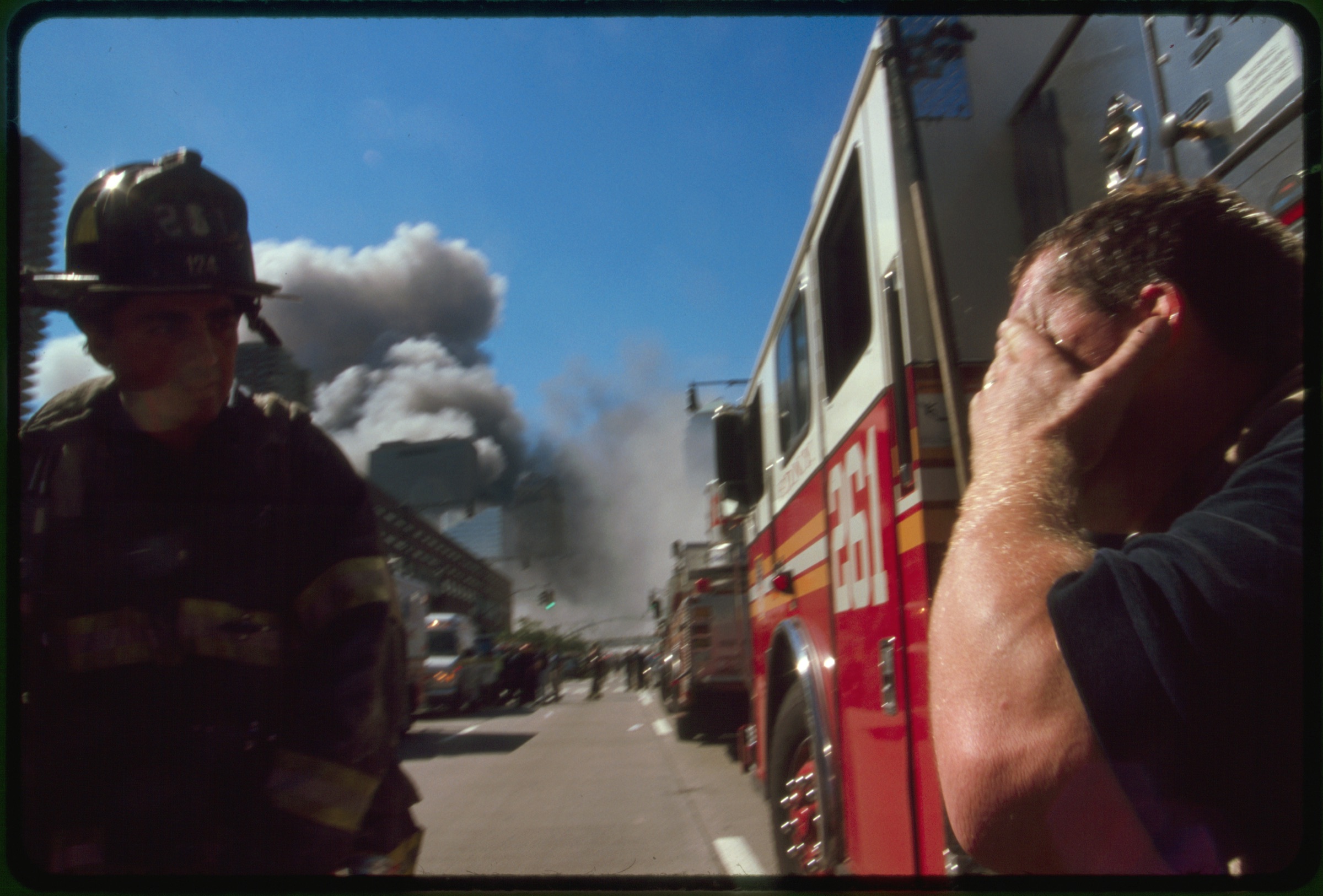 New York City fire fighter and another man covering his eyes on street in front of burning buildings following September 11th terrorist attack on World Trade Center, New York City