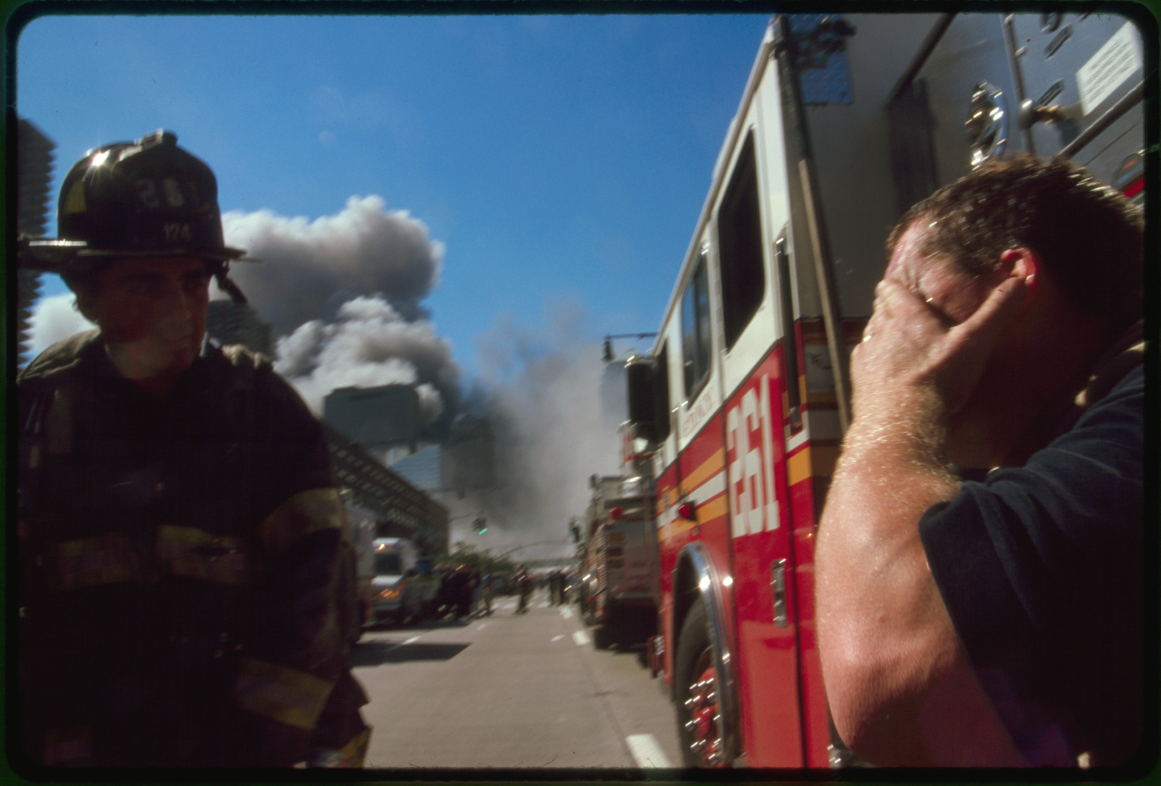 New York City fire fighter and another man covering his eyes on street in front of burning buildings following Septmber 11th terrorist attack on World Trade Center, New York City