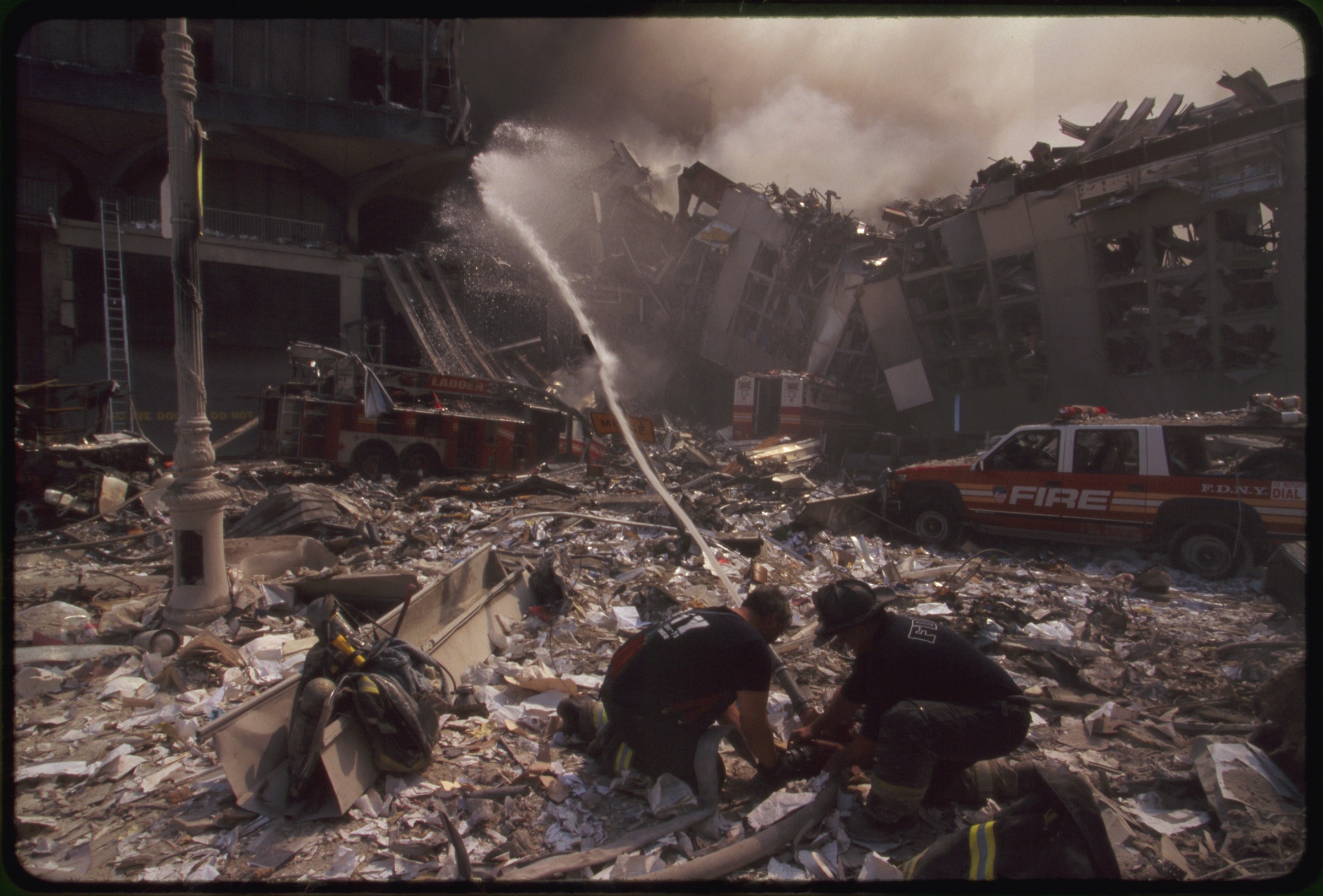 Two New York City fire fighters spraying water on smoldering ruins following September 11th terrorist attack on World Trade Center, New York City