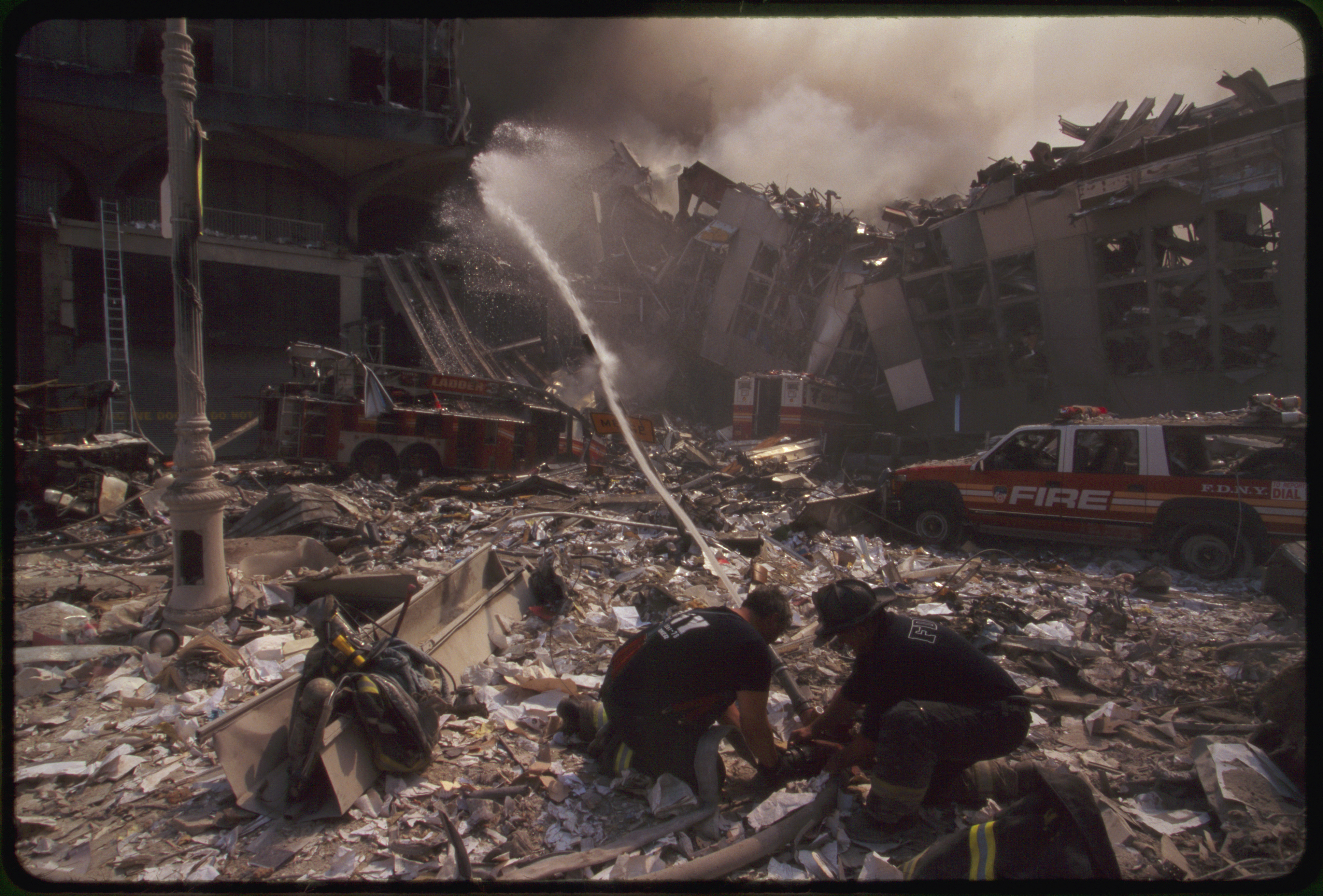 Two New York City fire fighters spraying water on smoldering ruins following September 11th terrorist attack on World Trade Center, New York City