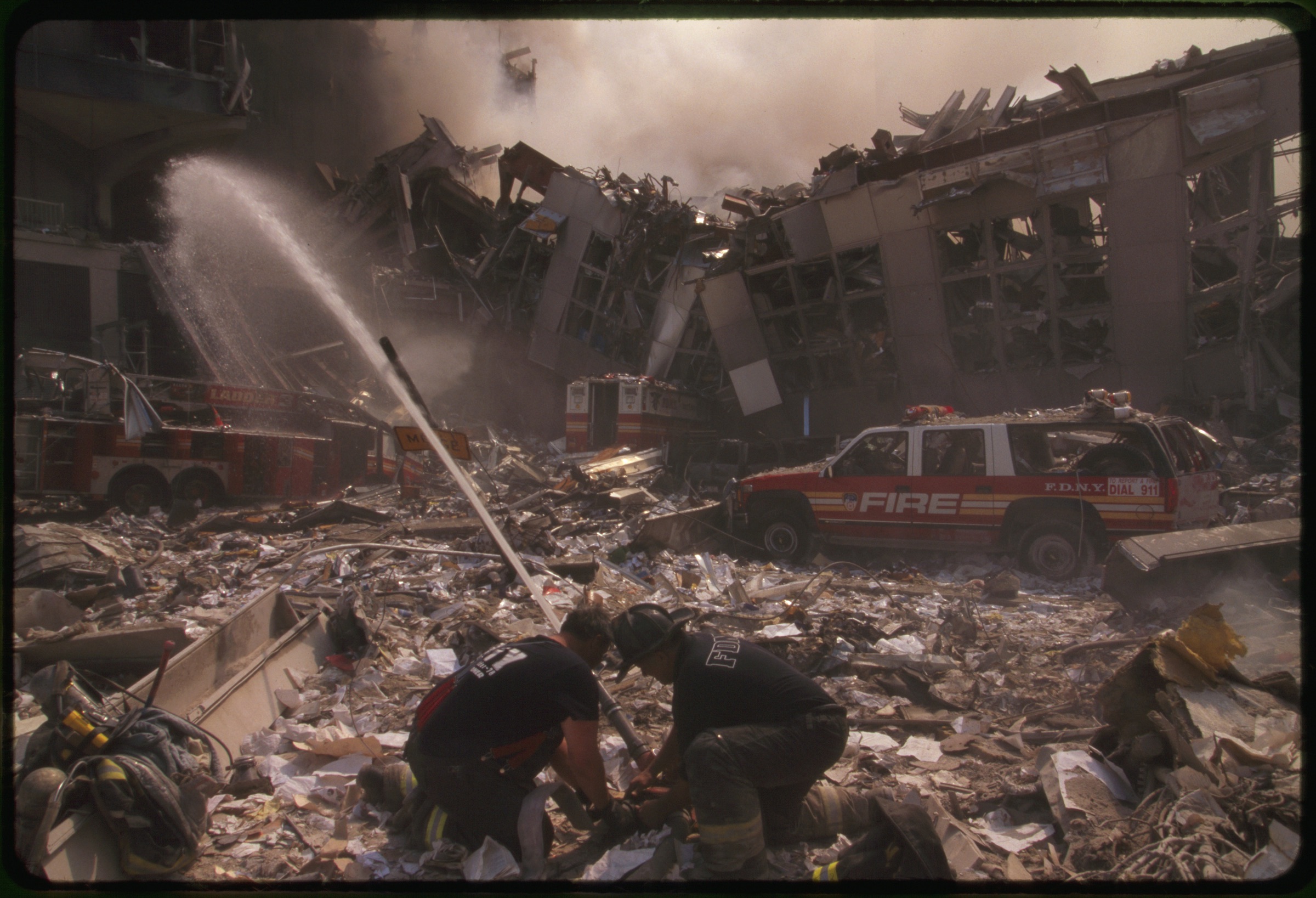 Two New York City fire fighters spraying water on smoldering ruins following September 11th terrorist attack on World Trade Center, New York City